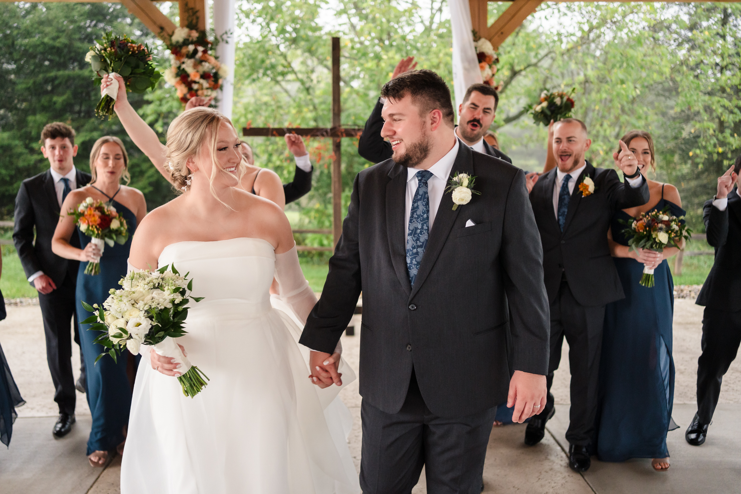 A bride and groom hold hands and walk down the aisle as their wedding party celebrates behind them