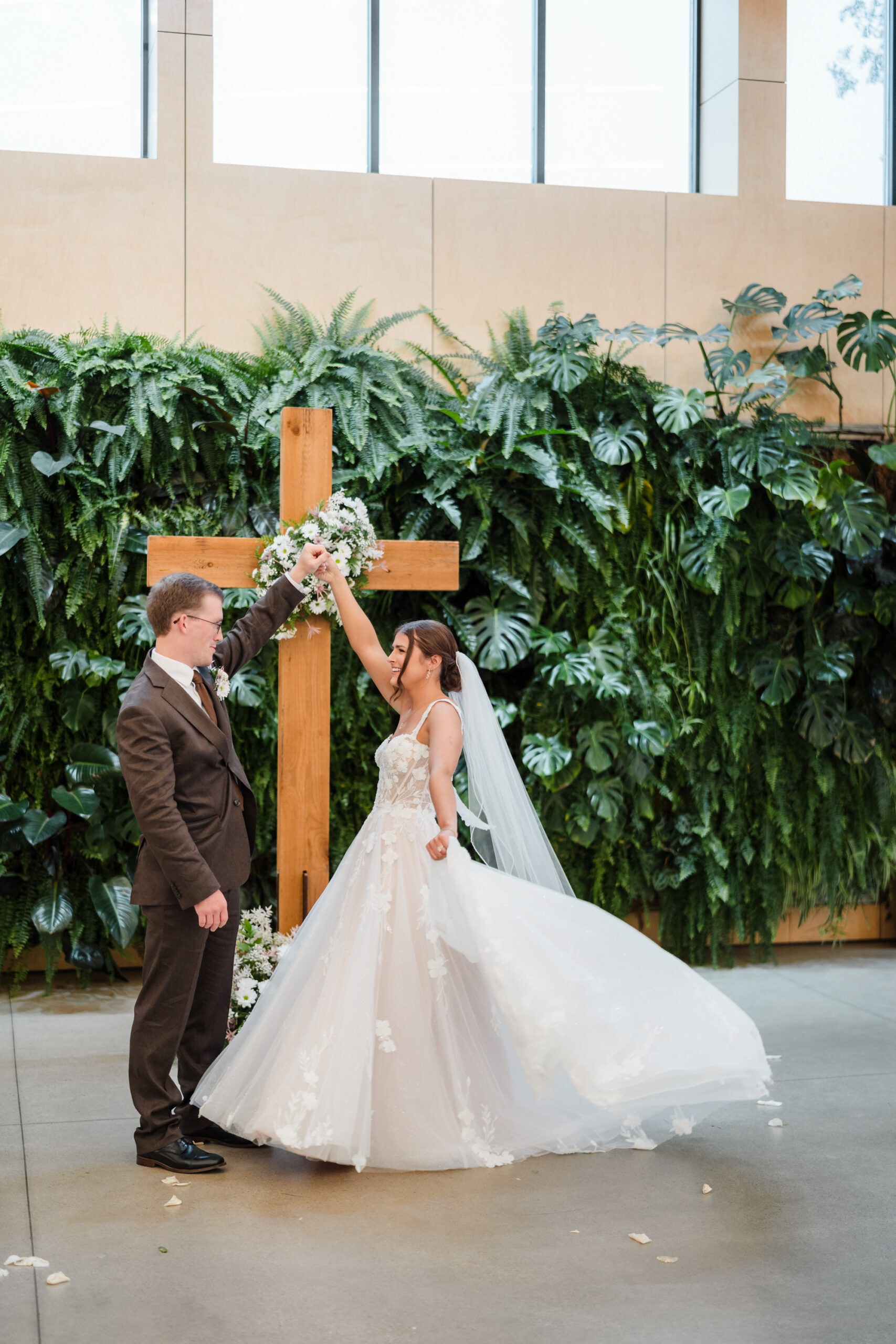 A groom spins his bride in front of a cross inside the ceremony space of Jorgensen Farms Gardens